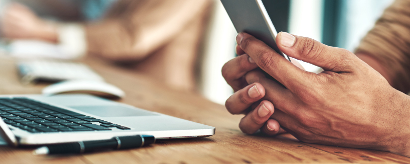 hands holding mobile phone with computer on desk